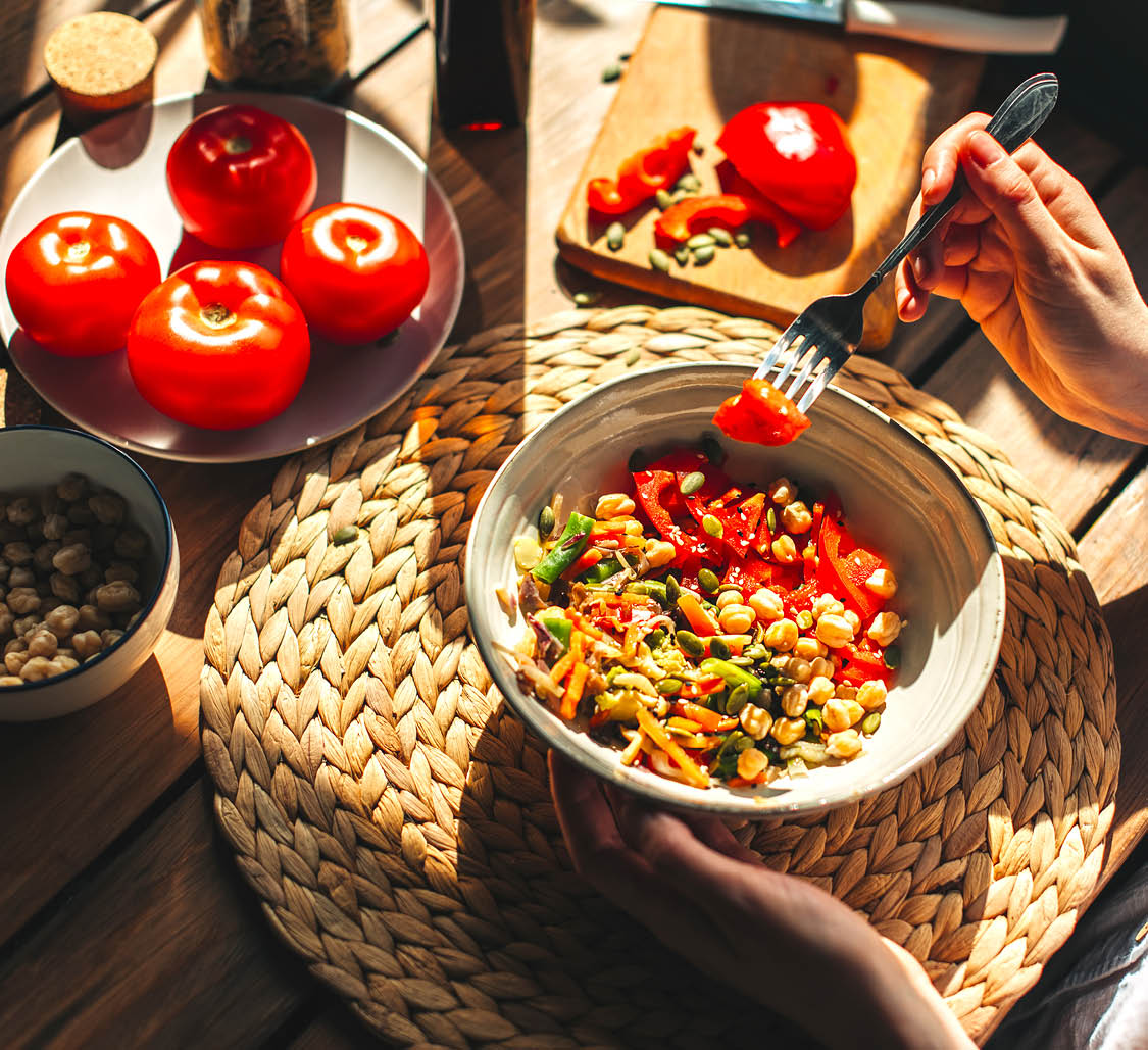 Young woman eating healthy food sitting in the beautiful interior with green flowers on the background