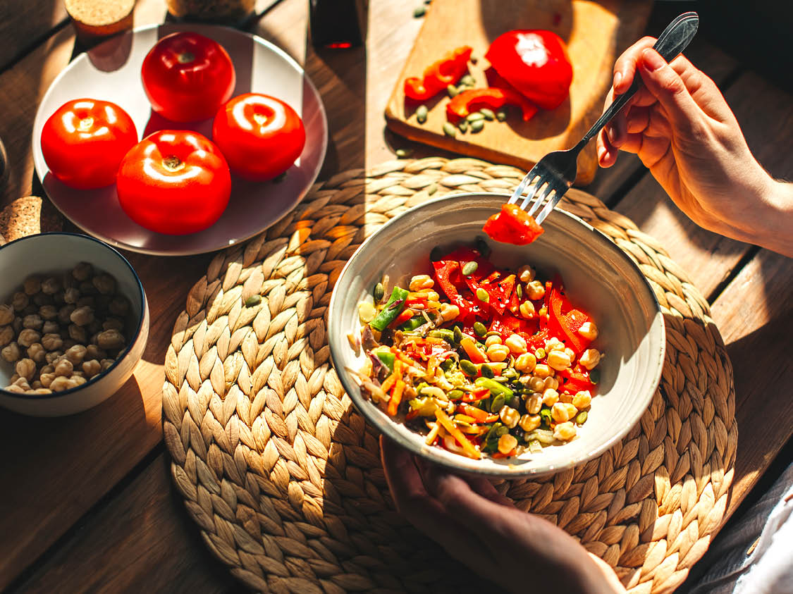 Young woman eating healthy food sitting in the beautiful interior with green flowers on the background